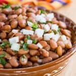 A terracotta dish of beans sprinkled with chopped onion and cilantro with text overlay that says "Instant Pot Pinto Beans".