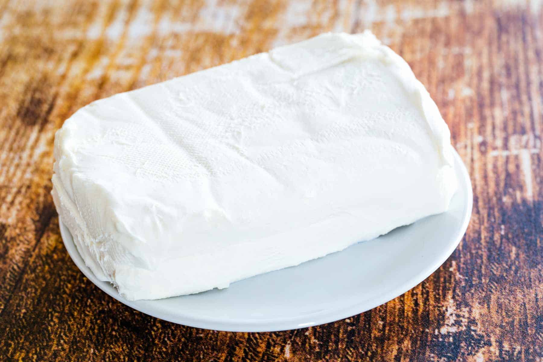 A bar of cream cheese on a small white plate.