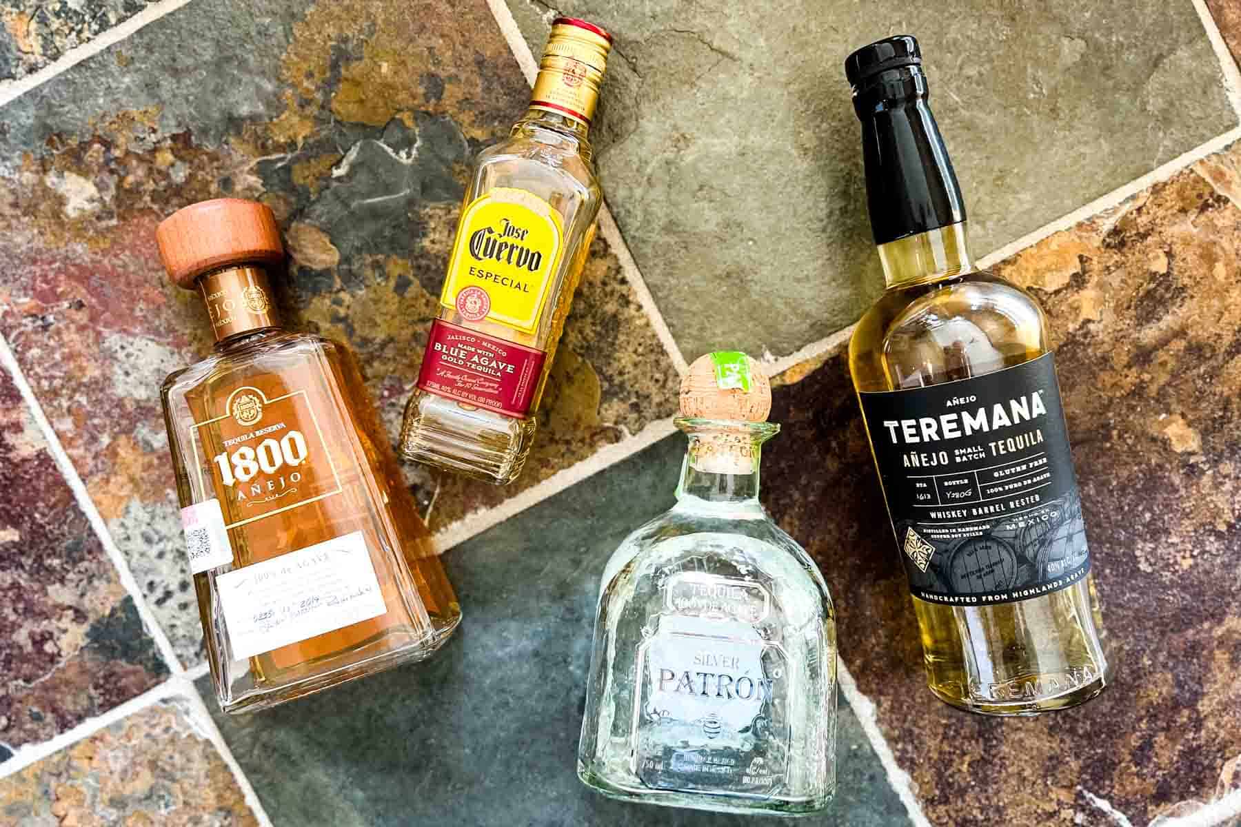 Four bottled of different brands of tequila lying on a stone tile surface.