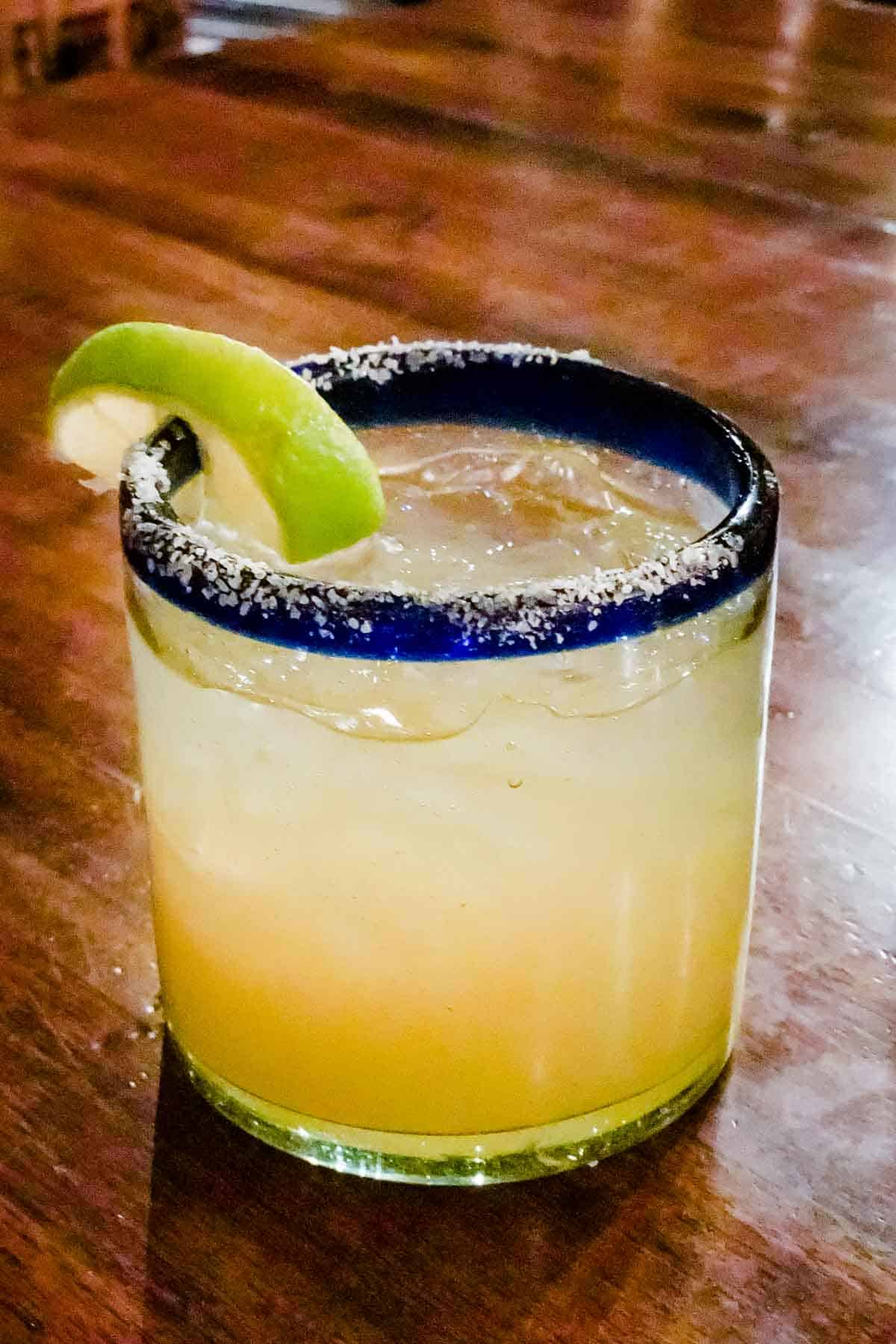 A margarita garnished with a lime on a dark wood table.