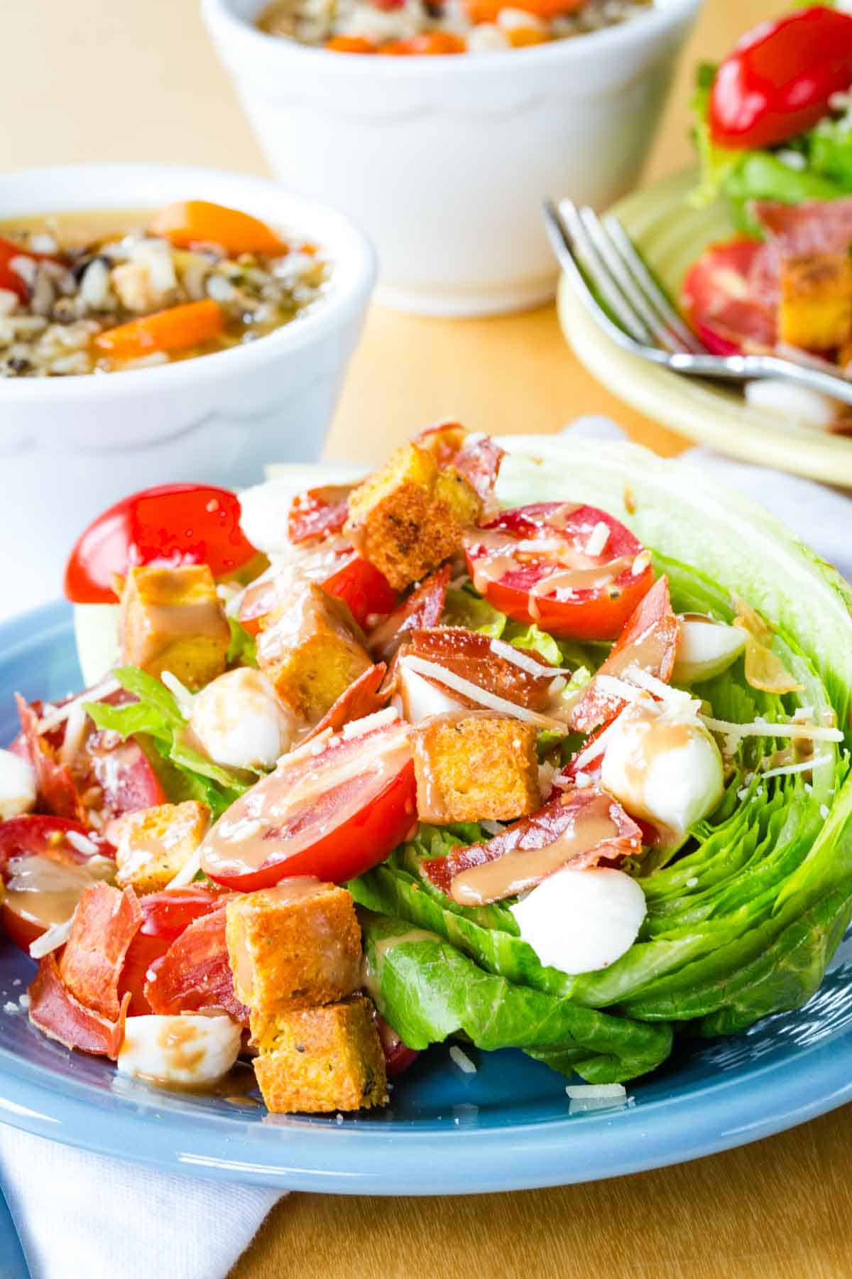 A wedge salad made with Romaine salad topped with fresh mozzarella, tomatoes, and crispy prosciutto.