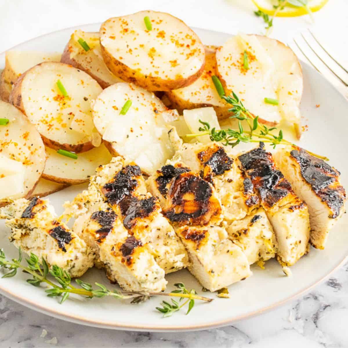 A sliced Lemon Herb Grilled Chicken Breast served on a white plate with potato slices.