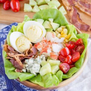 Lobster Cobb Salad with bacon, avocado, tomatoes, corn, blue cheese, and deviled eggs in a wooden bowl.