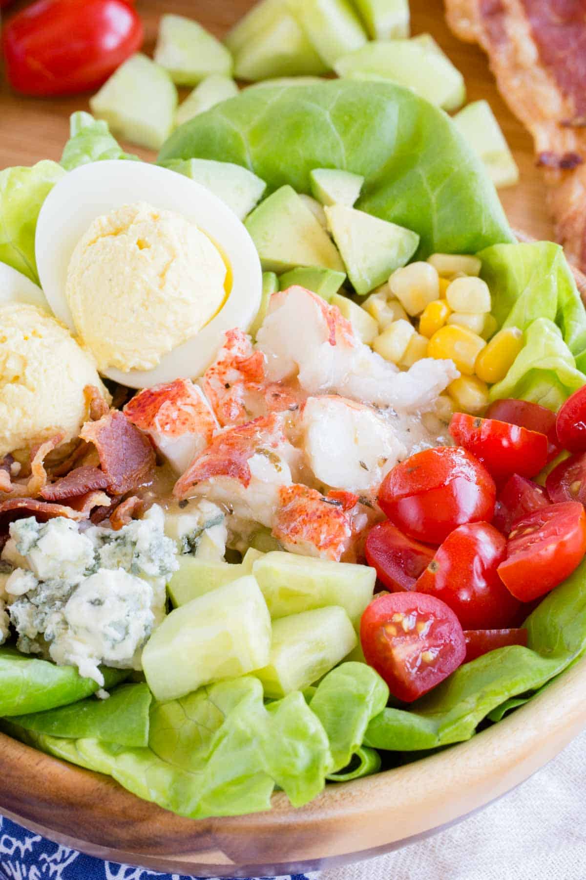 A closeup of the lobster, bacon, tomatoes, cucumber, blue cheese, and other toppings on the lettuce.