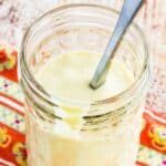 A spoon in a jar of salad dressing with text overlay that says "Creamy Maple Dijon Dressing".