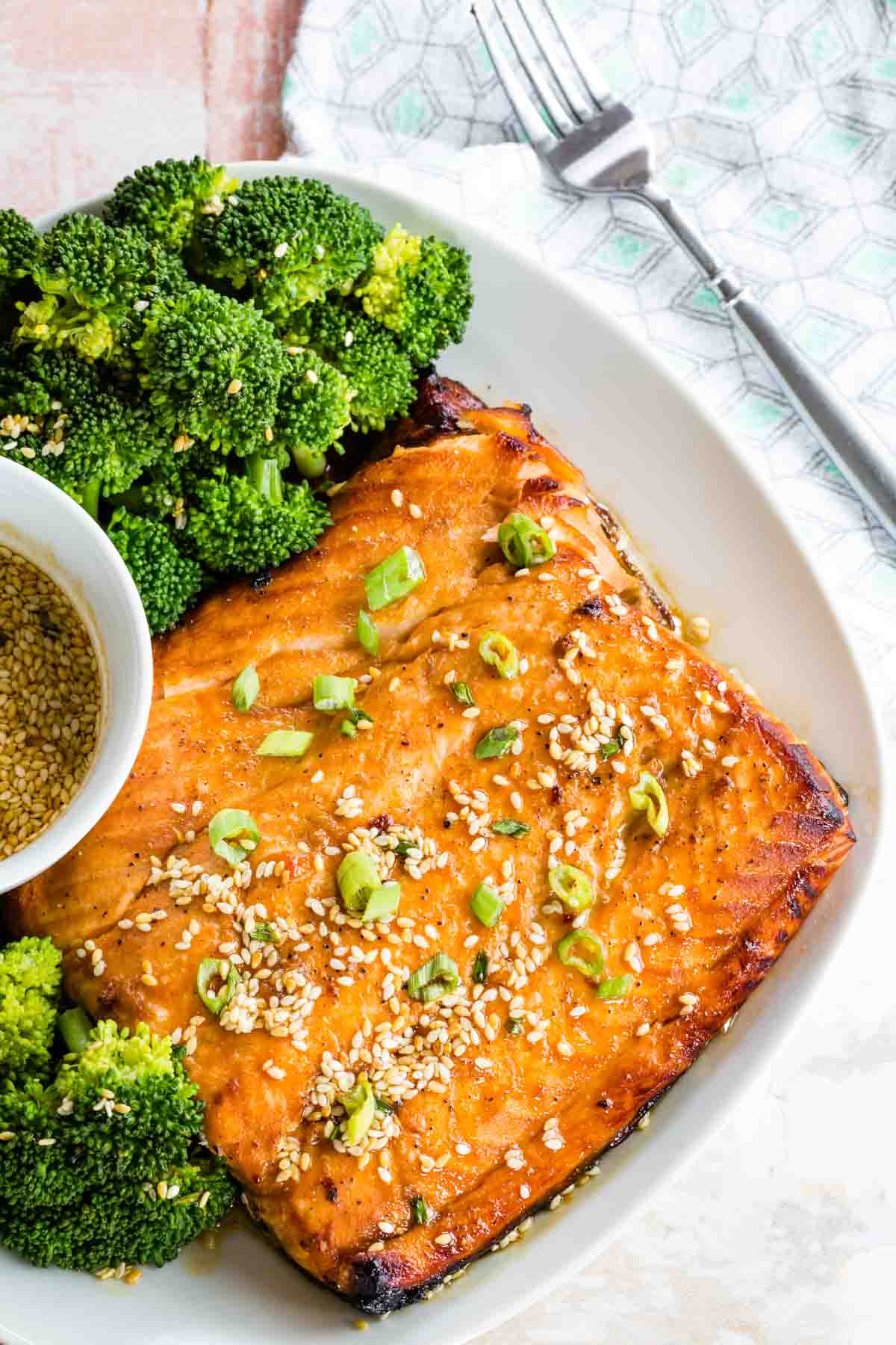 A birds eye view of a piece of broiled Salmon and broccoli with a bowl of Sesame Maple Glaze and a fork next to it.