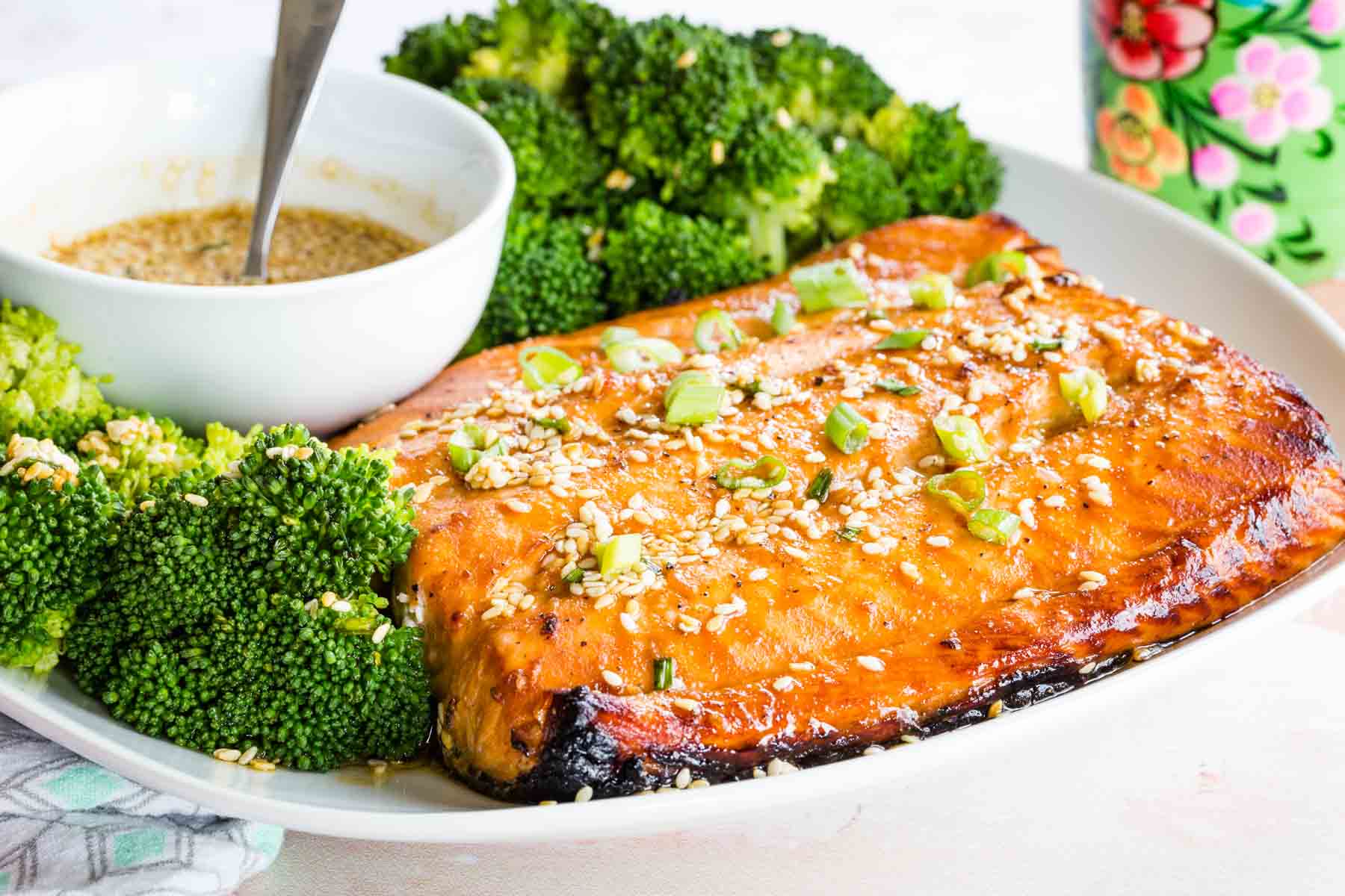 Maple glazed salmon plated with steamed broccoli and a bowl of maple sesame sauce.