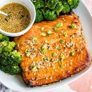 A birsdw eye view of a plate of maple glazed salmon with broccoli and a bowl of extra sauce.