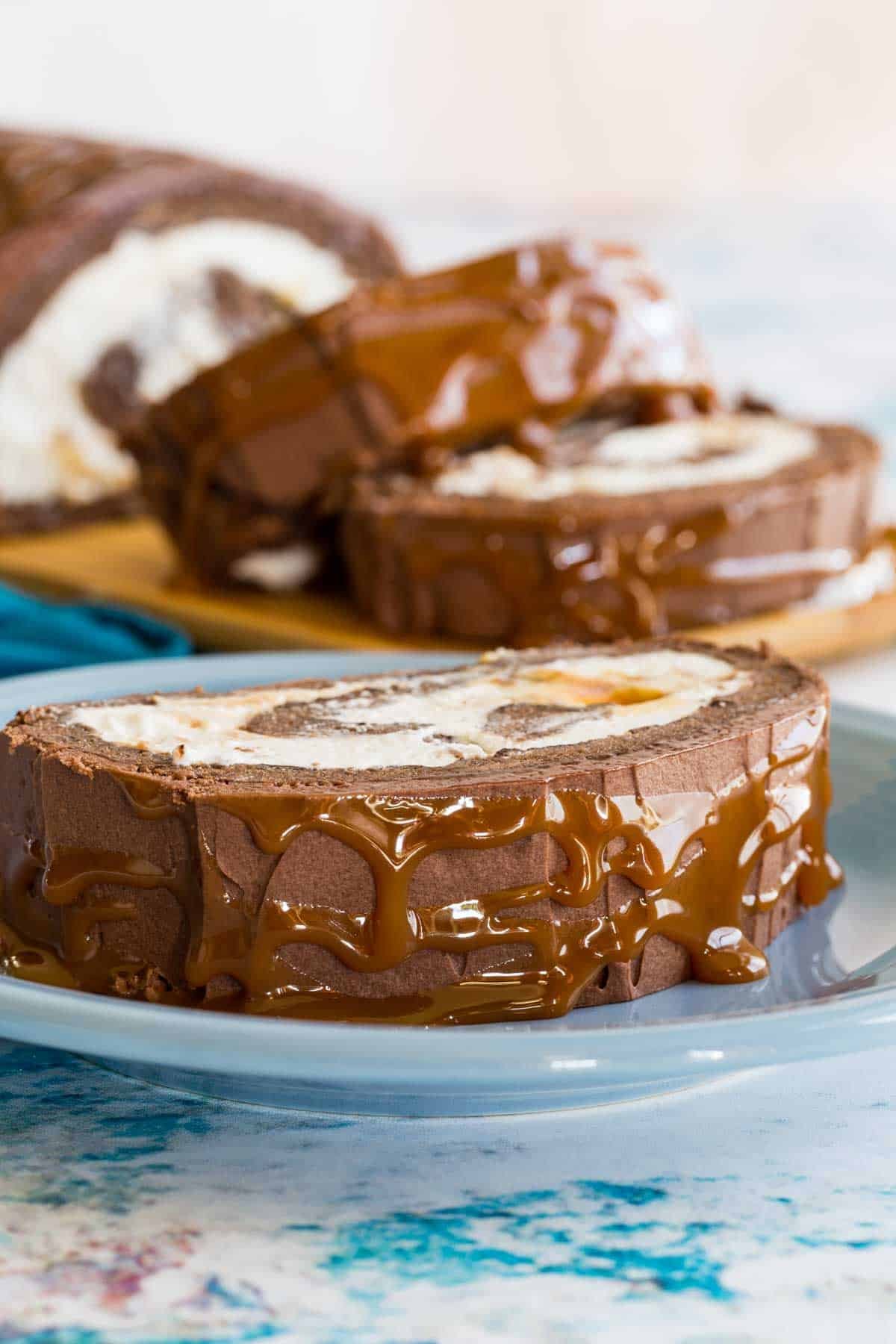 A slice of chocolate roll cake filled with whipped cream and drizzled with caramel.
