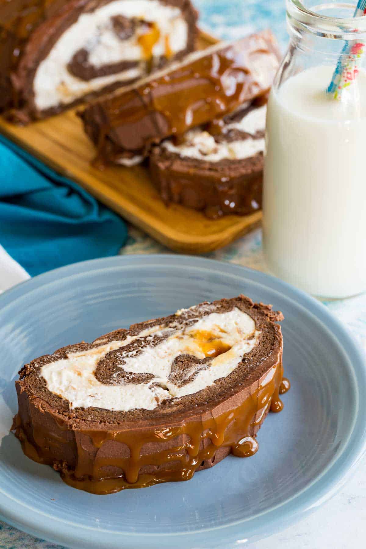 A piece of Caramel Swiss Roll with whipped cream filling and dripping with caramel on a plate.