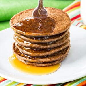 A stack of mini chocolate pancakes covered in syrup on a small white plate.