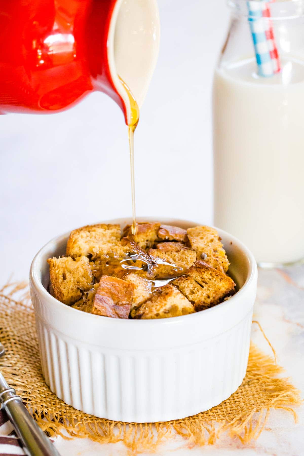 Pouring syrup from a red jug onto a French Toast bake in a ramekin.