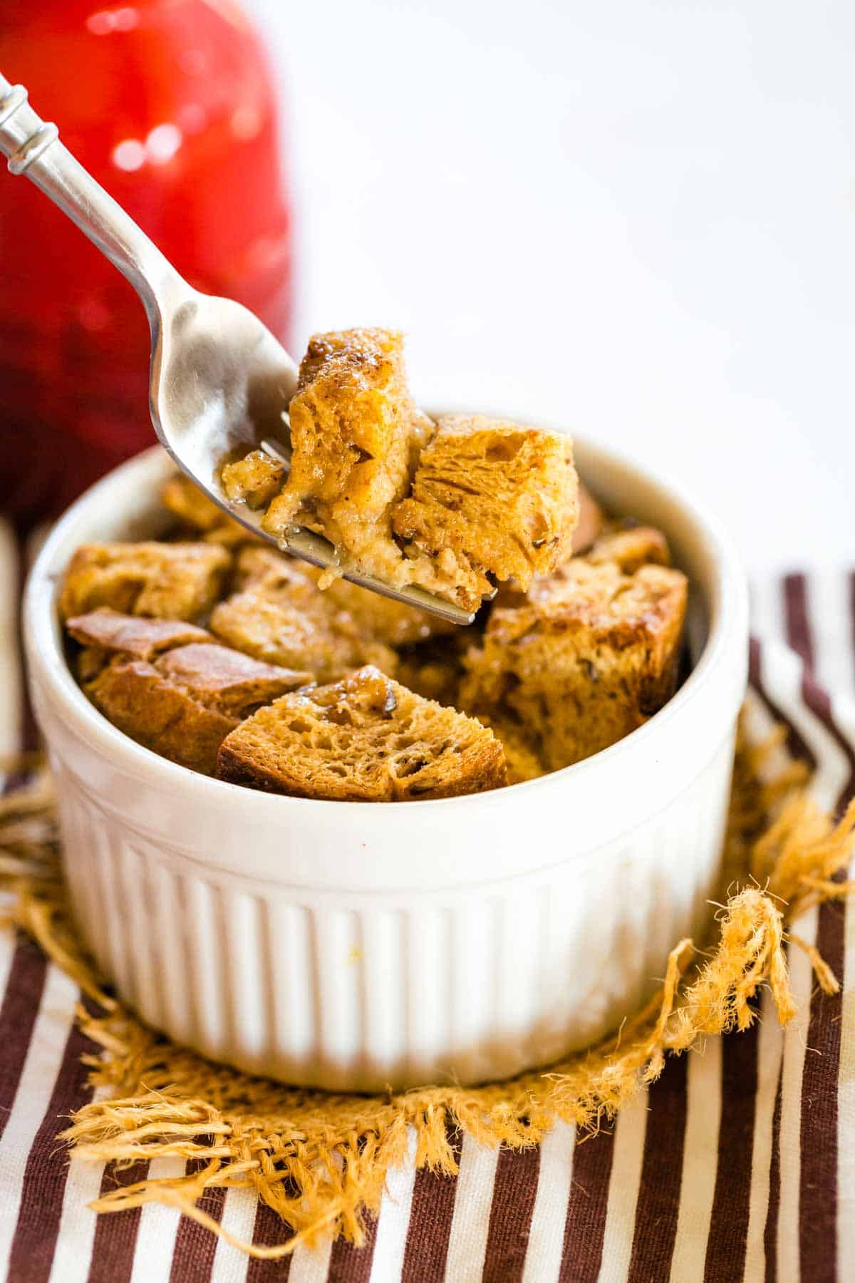 A fork picking up a bite of French toast from a ramekin.