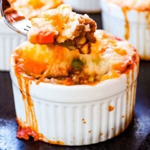 A fork picking up a bite out of a mini shepherd's pie in a ramekin.