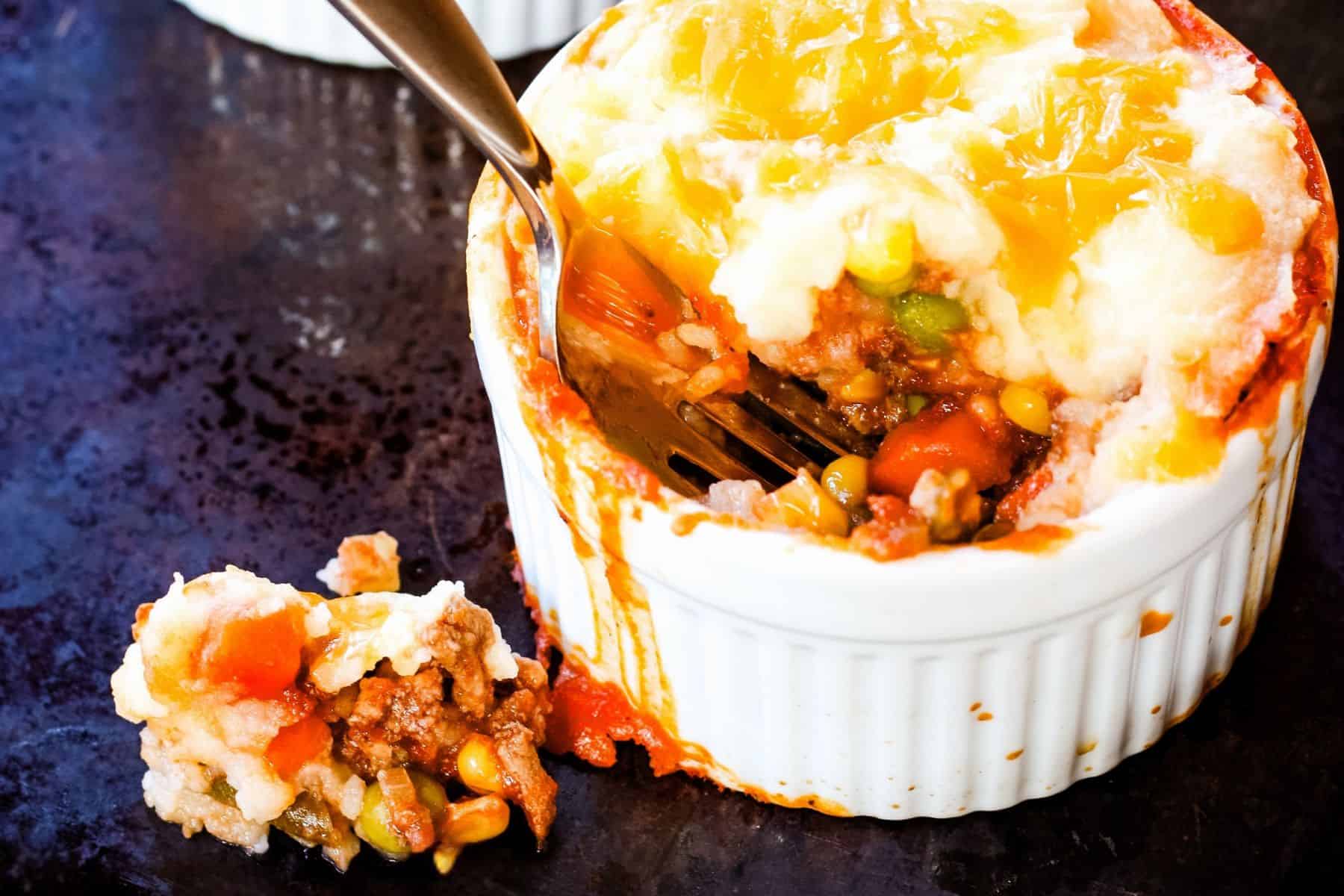 A fork in a mini shepherd's pie with a bite that fell out next to the ramekin.