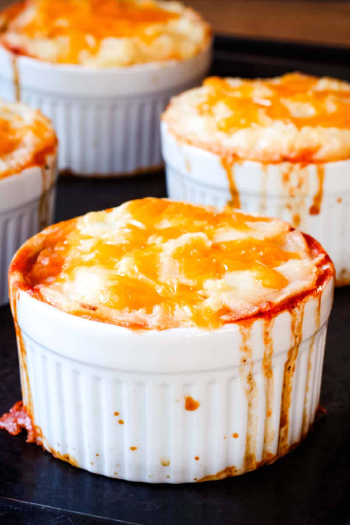 A closeup of the mashed potato and cheese topping in a ramekin with some filling dripping down the sides.