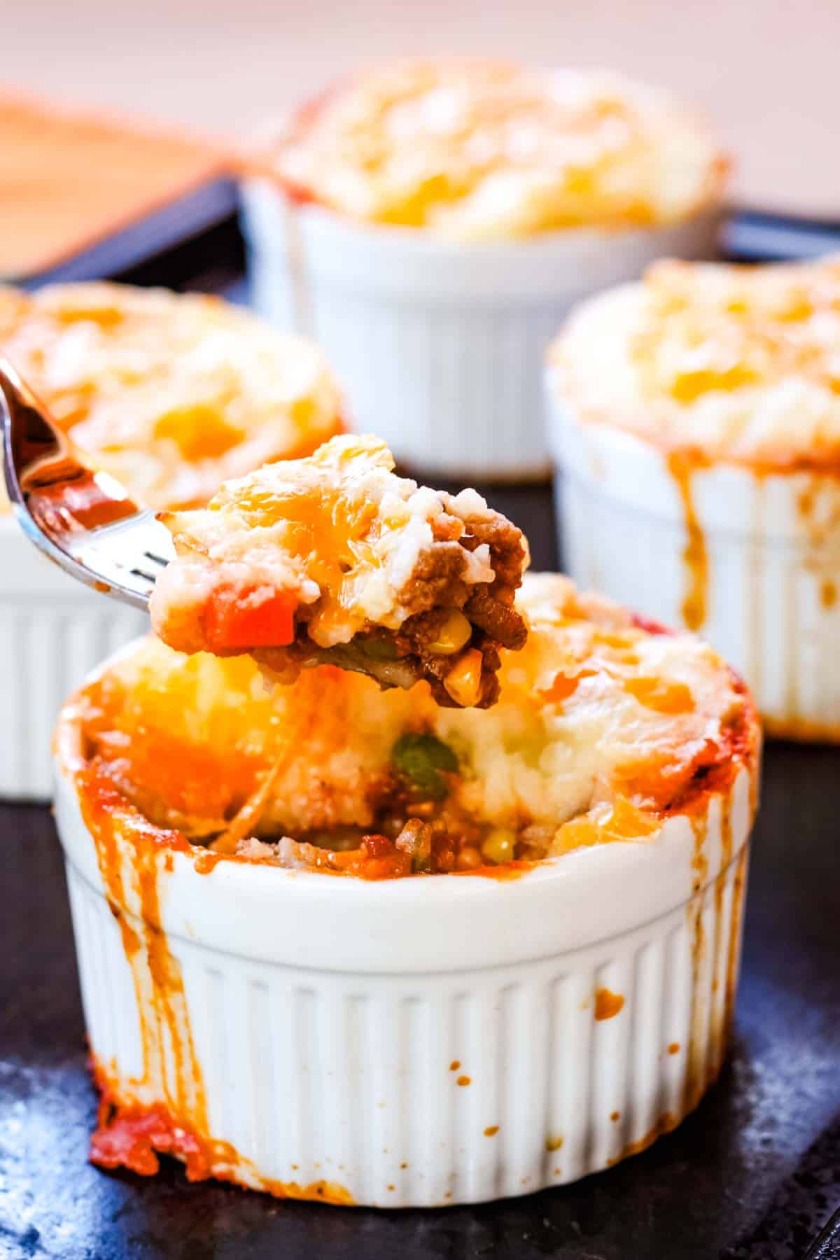 A fork picking up a bite or beef, veggies, and mashed potatoes from a mini shepherd's pie.