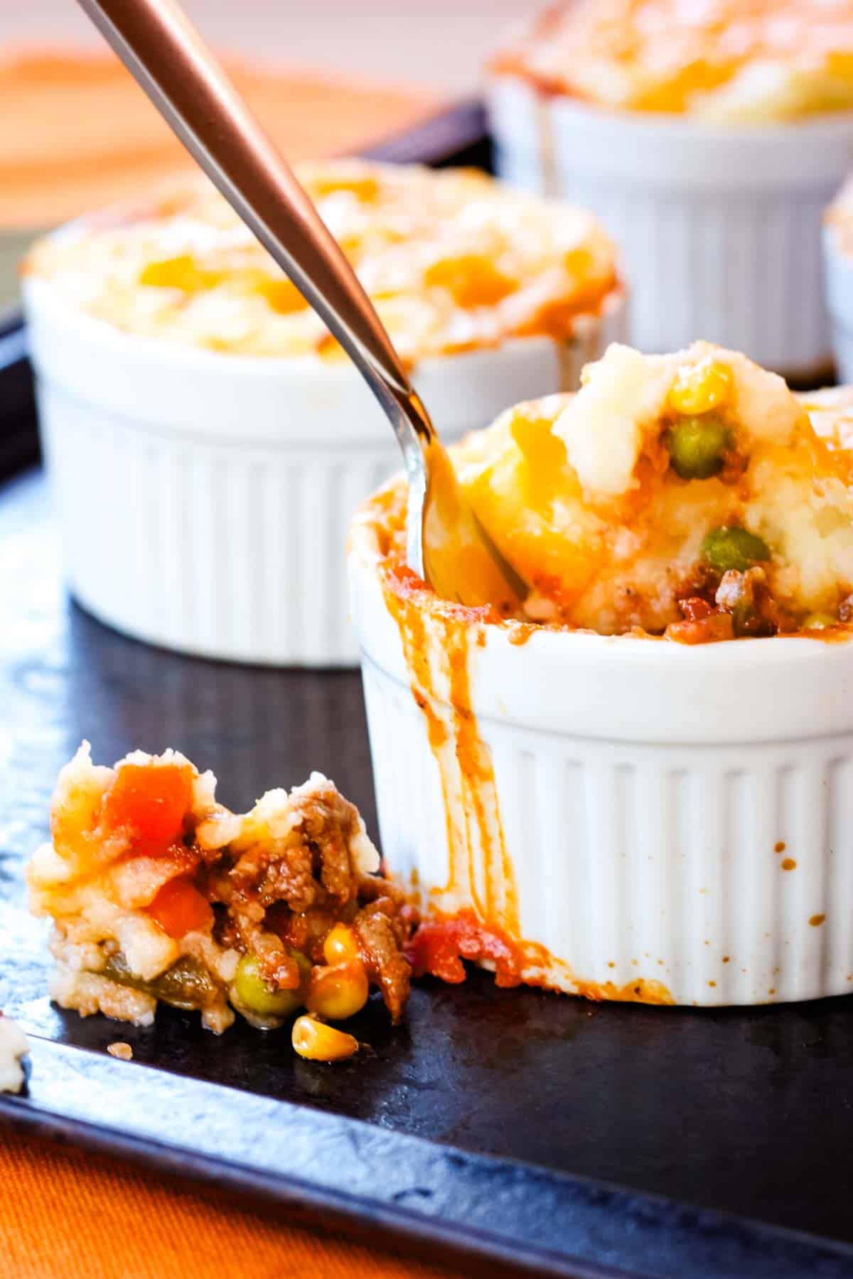 Ramekins of mini shepherd's pies on a baking sheet with some spilling out of the one with a fork in it.