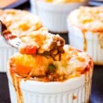 A fork picking up a bite of meat and potatoes out of a ramekin with text overlay that says "Mini Shepherd's Pie".