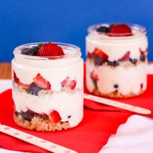 Two mixed berry quinoa parfaits with yogurt in jars on red napkins.