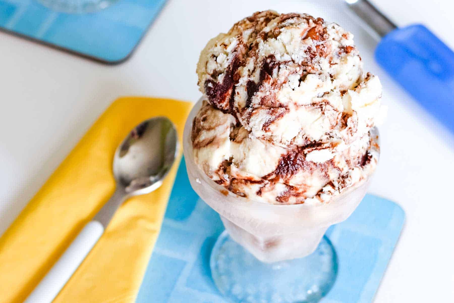 Ice cream with chocolate swirls in a glass sundae bowl and a spoon on a yellow napkin.