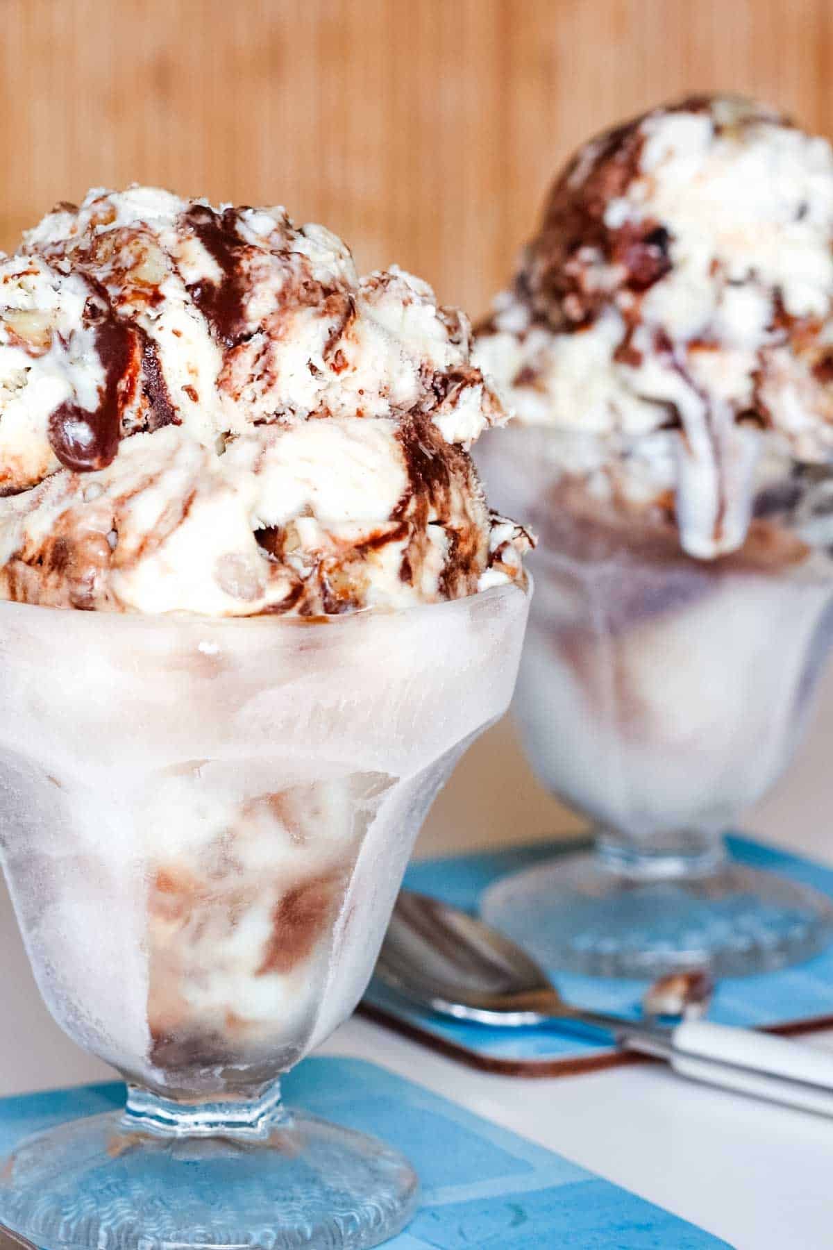 A closeup of a glass sundae dish of butter pecan fudge ripple ice cream.