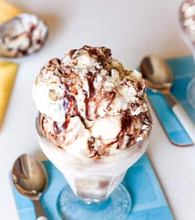 A dish of fudge swirl ice cream on a blue coaster with a spoon next to it.