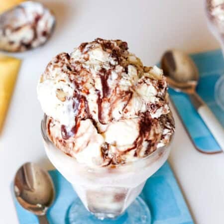 A dish of fudge swirl ice cream on a blue coaster with a spoon next to it.
