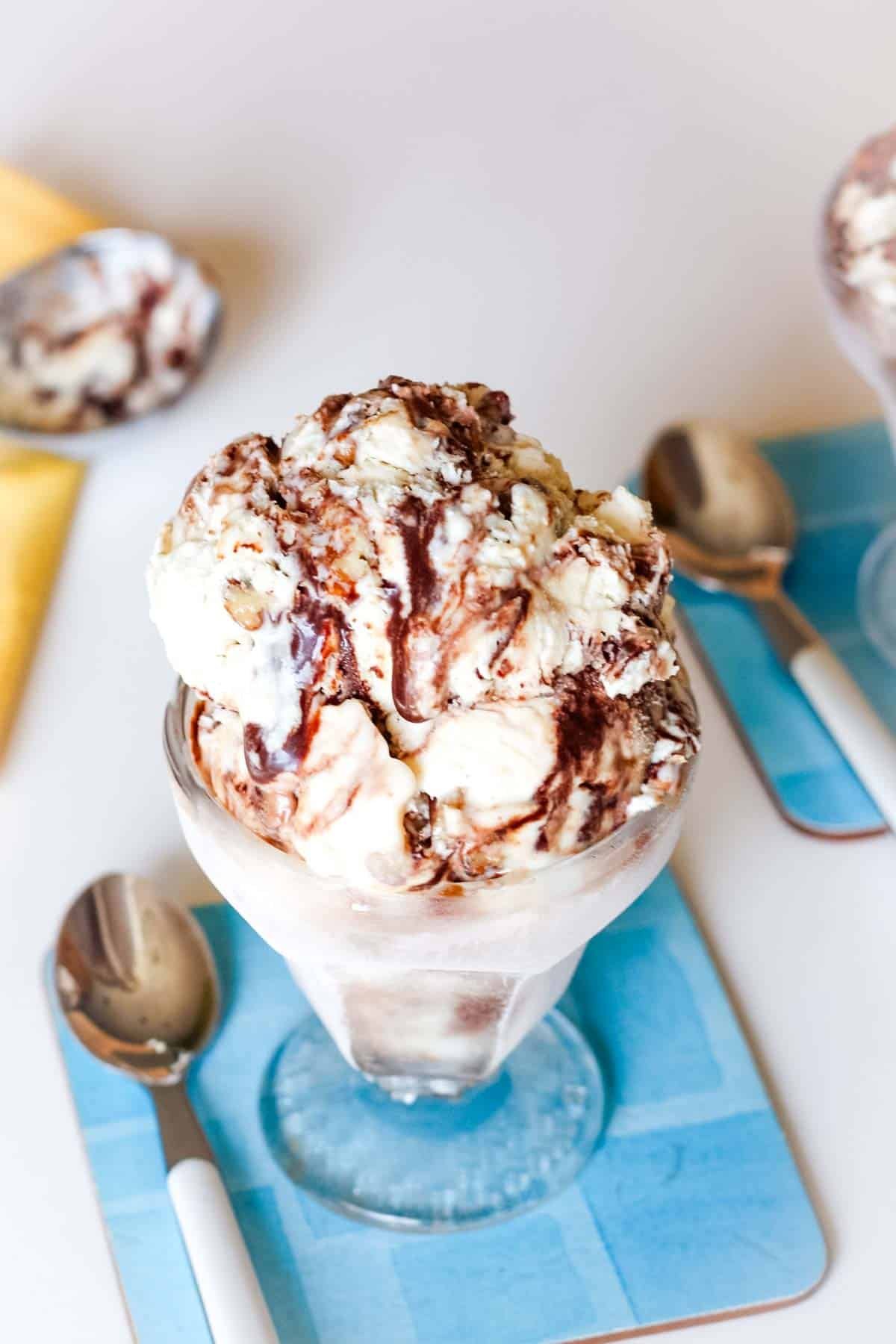 A dish of fudge swirl ice cream on a blue coaster with a spoon next to it.