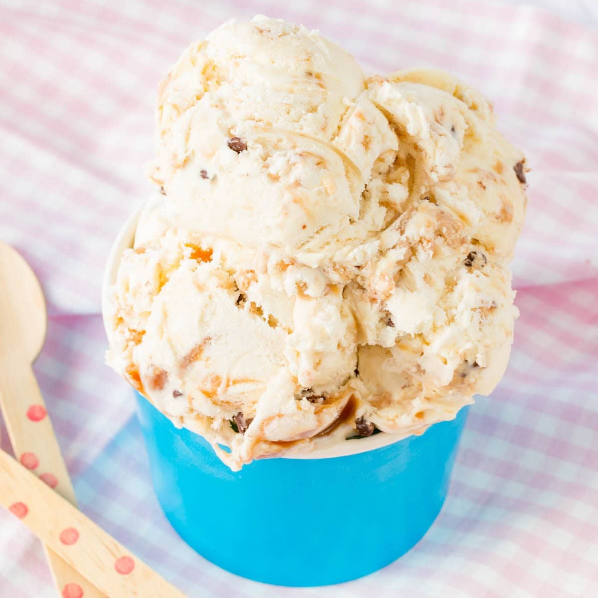 A bowl of ice cream with caramel, toffee, chocolate chips and a spoon next to it.