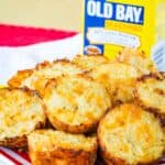 Cauliflower tots piled on a striped plate with a container of Old Bay Seasoning in the background.