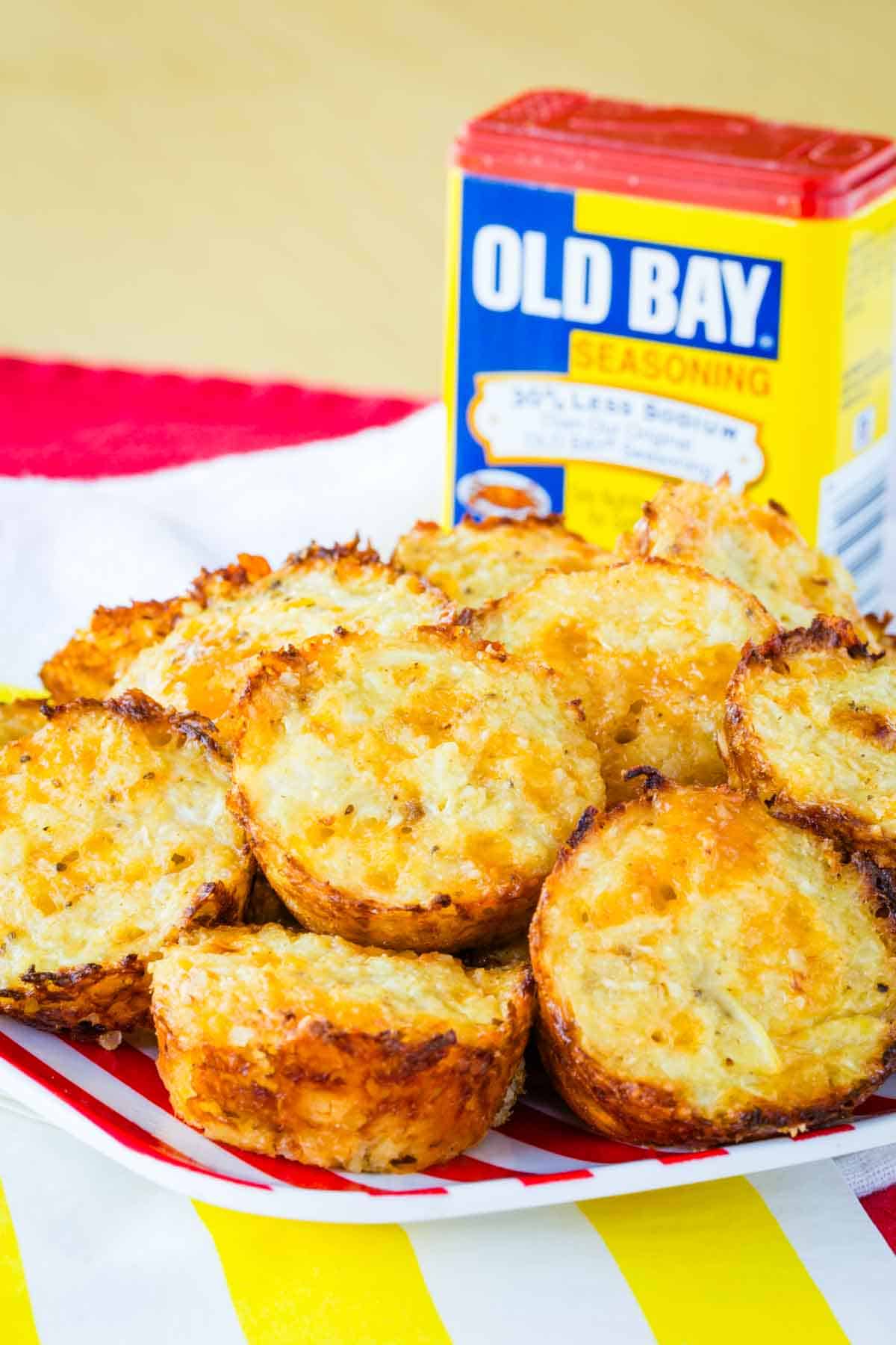 Cauliflower tots piled on a striped plate with a container of Old Bay Seasoning in the background.