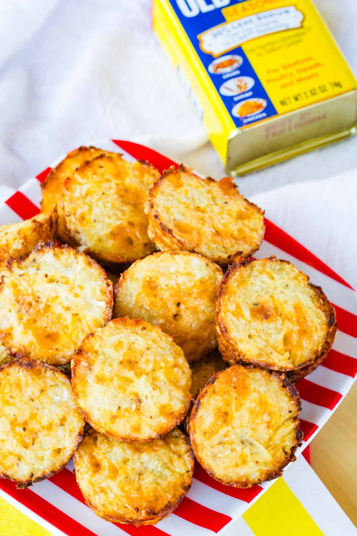 A plate of cauliflower tots and a tin of Old Bay seasoning on top of napkins on a table.