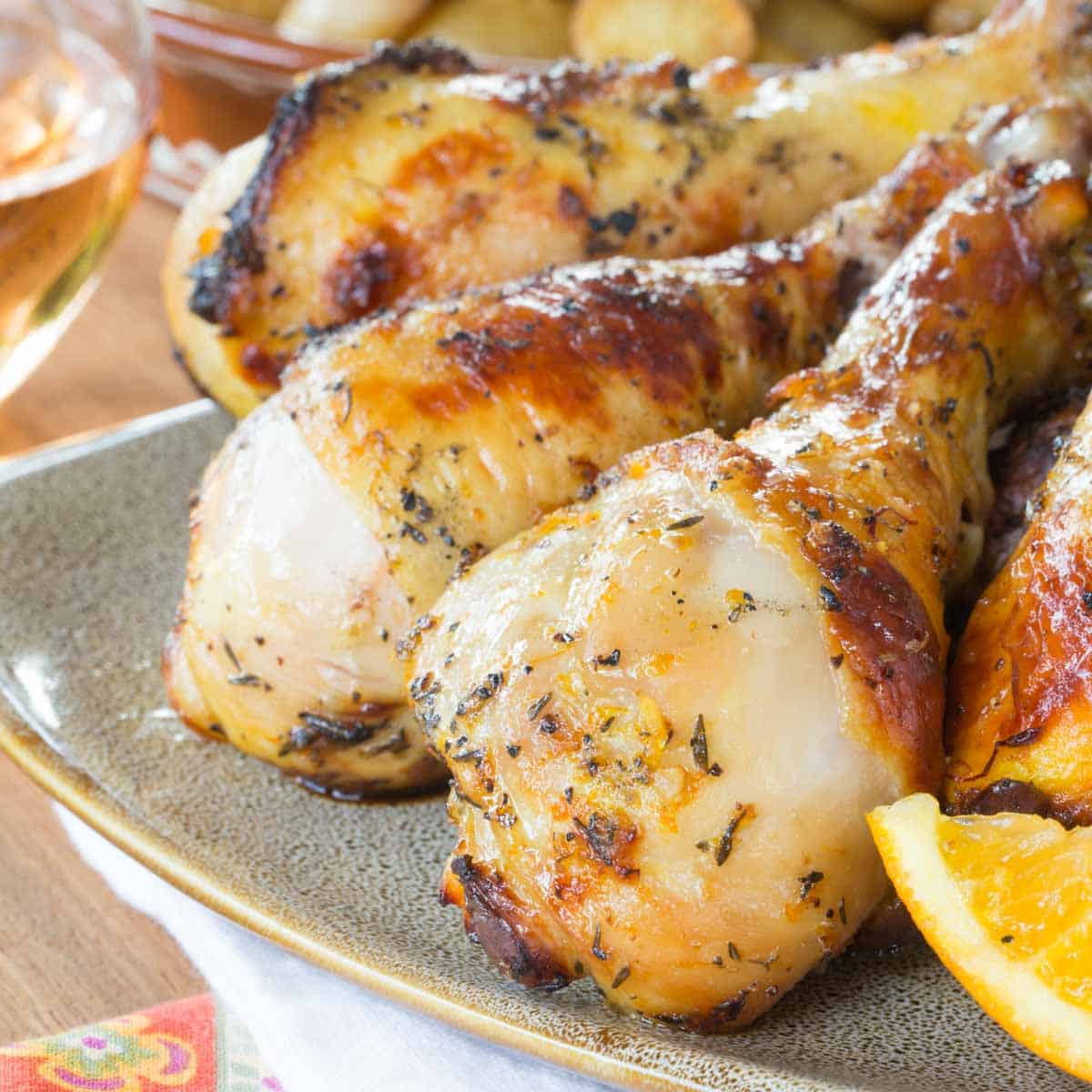 Grilled chicken legs with the caramelized orange saffron marinade on the exterior on a tan plate.