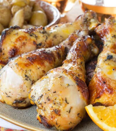 Juicy citrus marinated chicken drumsticks on a platter with glasses of wine in the background.