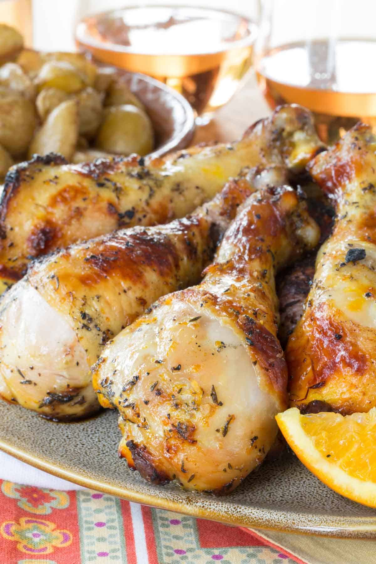 Juicy citrus marinated chicken drumsticks on a platter with glasses of wine in the background.