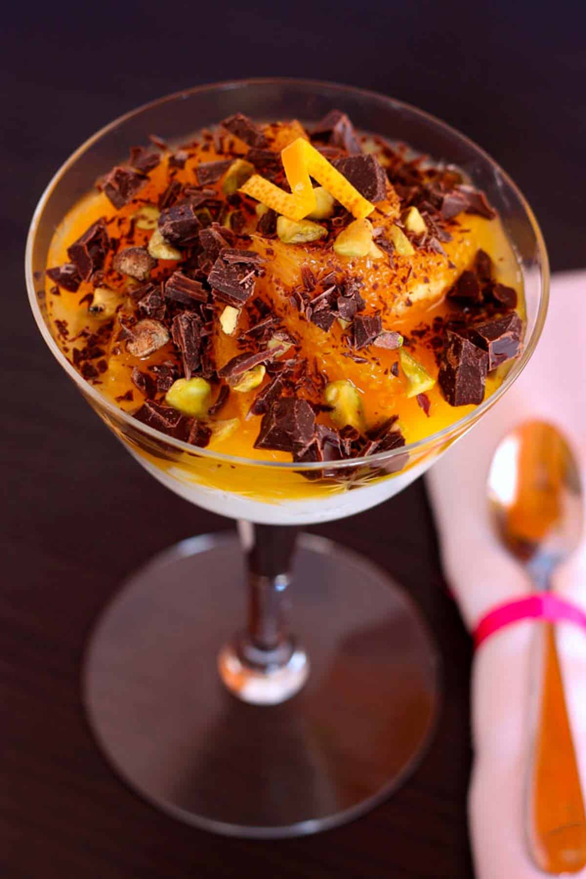 Looking down at an orange yogurt parfait topped with chopped pistachios and chocolate in a glass.