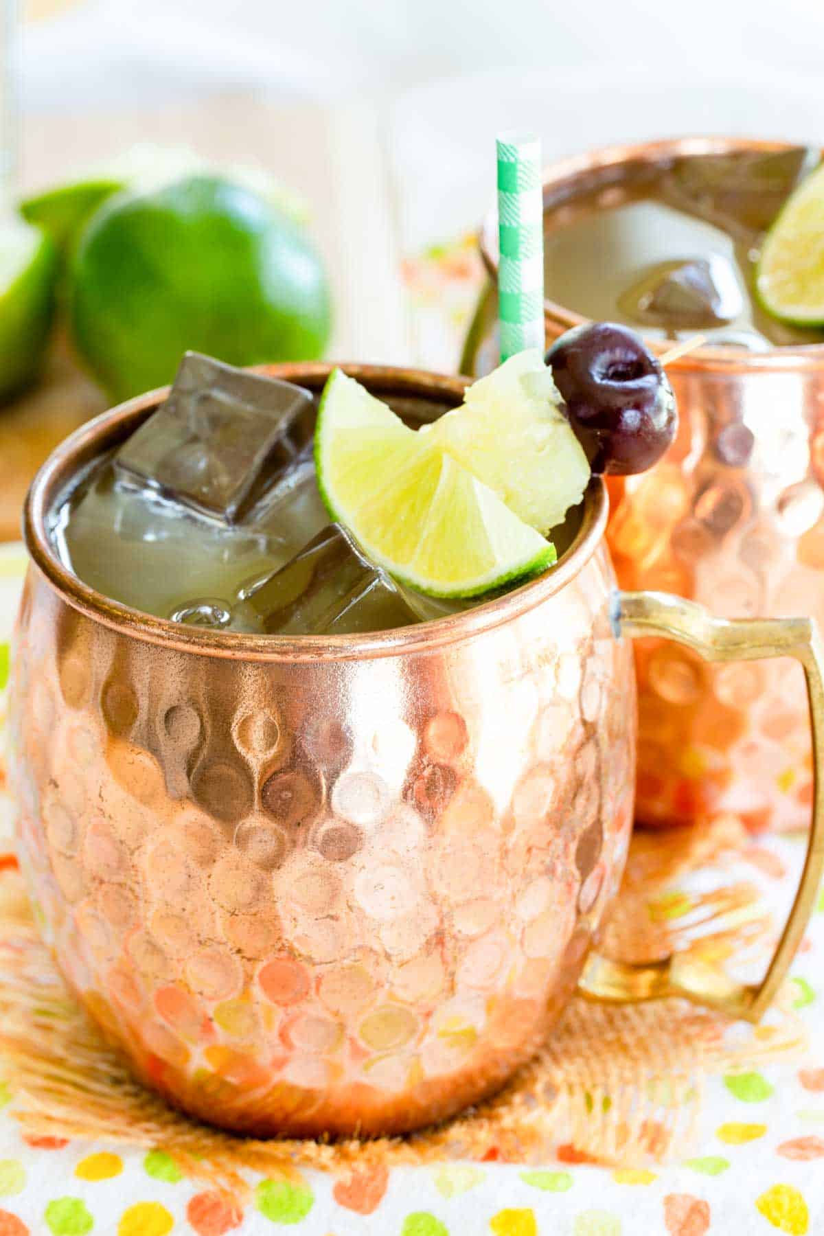 Two pina colada moscow mules with fruit garnish and a paper straw in copper mugs.