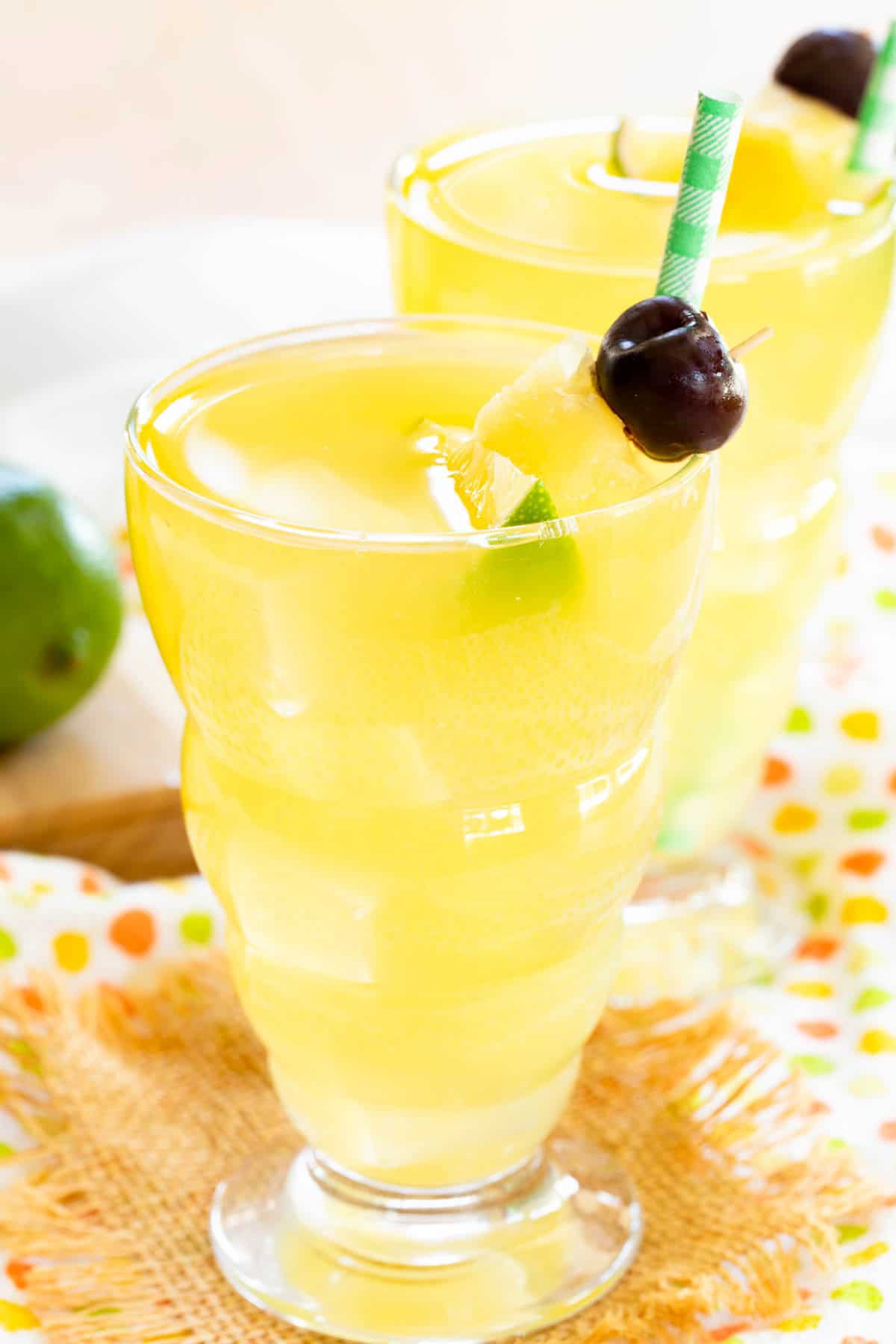 Two glasses of yellow drink with a straw and fruit garnish.