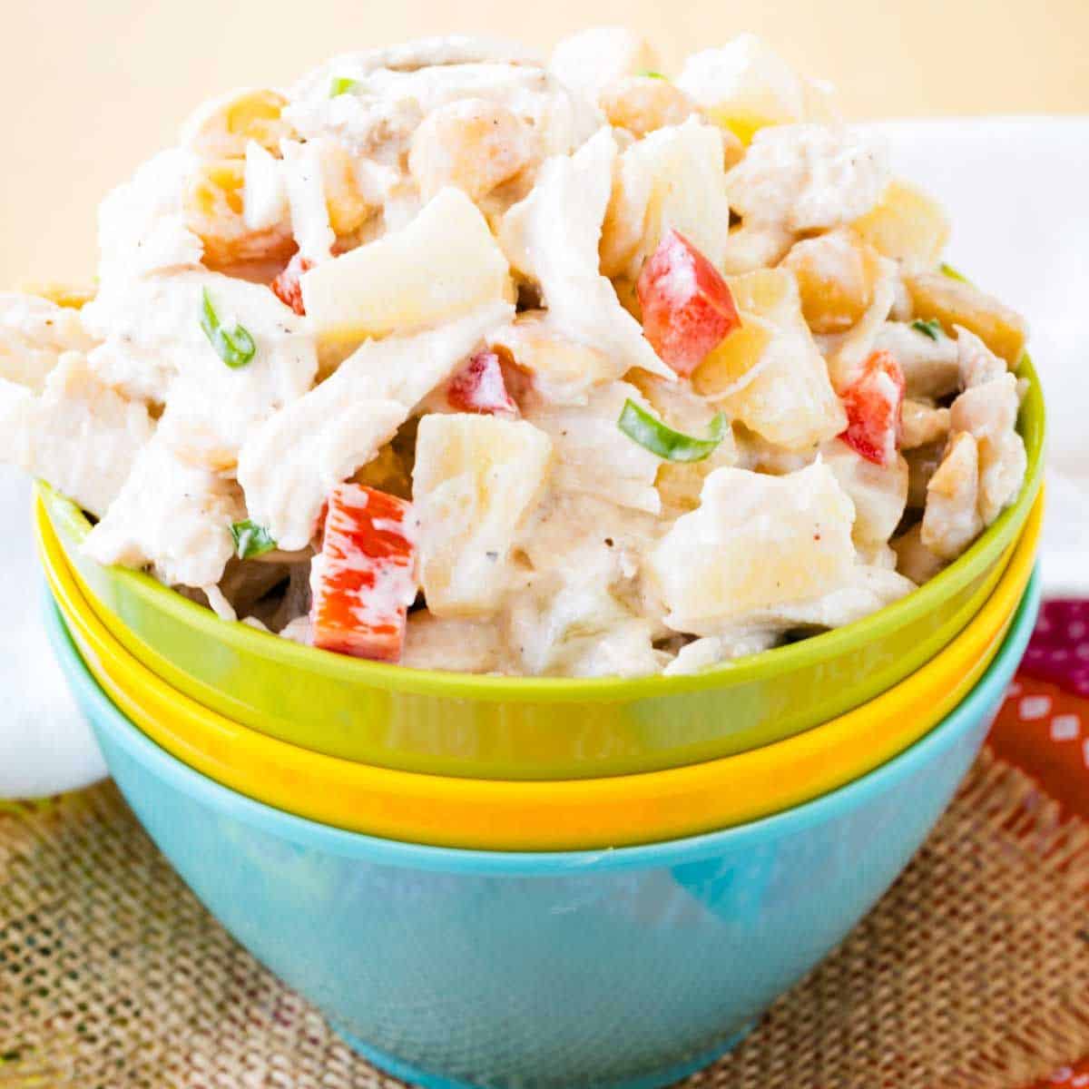 Three stacked multicolor bowls with the top green one full of pineapple chicken salad.
