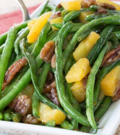 A closeup of a plate of glazed green beans with pineapple tidbits and pecans.