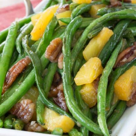 A closeup of a plate of glazed green beans with pineapple tidbits and pecans.