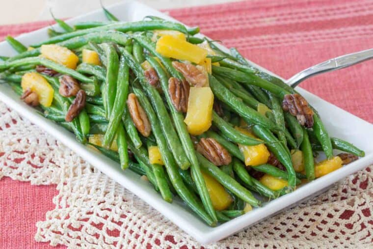 Pineapple green beans on a white serving dish with spoon in it.