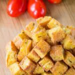 A closeup of polenta croutons with tomatoes in the background.