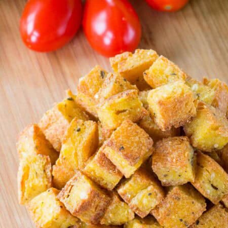 A closeup of polenta croutons with tomatoes in the background.