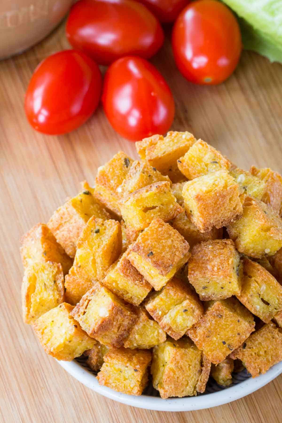 A closeup of polenta croutons with tomatoes in the background.