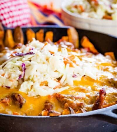 A closeup of a pan of pulled pork fries topped with melted cheese and coleslaw.