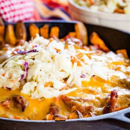 A closeup of a pan of pulled pork fries topped with melted cheese and coleslaw.