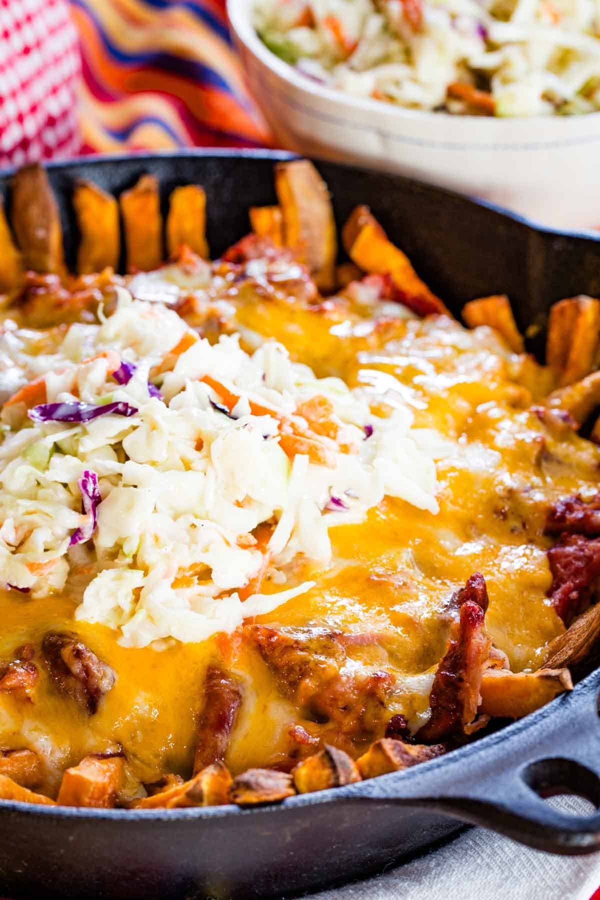 A closeup of a pan or sweet potato fries topped with barbecue pulled pork, melted cheese, and coleslaw.