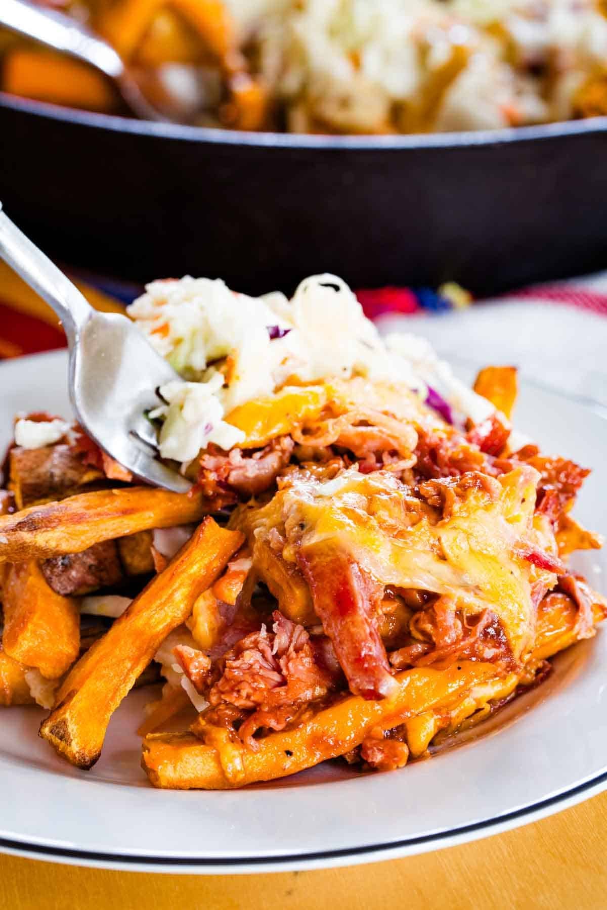 A fork digging in to a plate of loaded sweet potato fries.